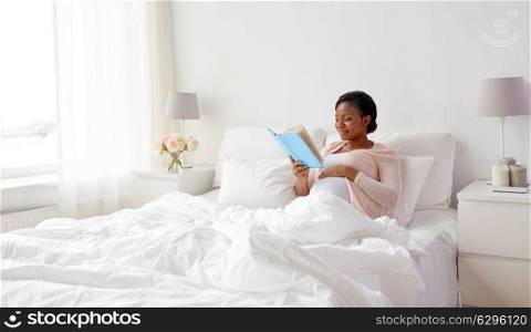 pregnancy and leisure concept - smiling pregnant african american woman reading book in bed at home. happy pregnant african woman reading book at home