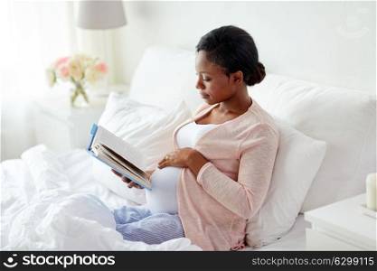 pregnancy and leisure concept - smiling pregnant african american woman reading book in bed at home. happy pregnant african woman reading book at home