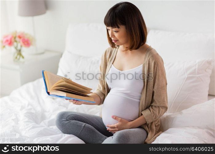 pregnancy and leisure concept - smiling pregnant asian woman reading book in bed at home. happy pregnant asian woman reading book at home