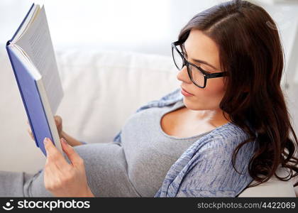 pregnancy and motherhood concept - pregnant woman lying on sofa and reading book. pregnant woman reading book at home