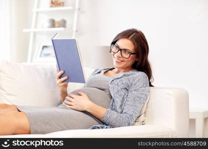 pregnancy and motherhood concept - smiling pregnant woman lying on sofa and reading book. happy pregnant woman reading book at home