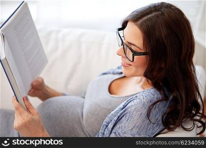 pregnancy and motherhood concept - smiling pregnant woman lying on sofa and reading book. happy pregnant woman reading book at home