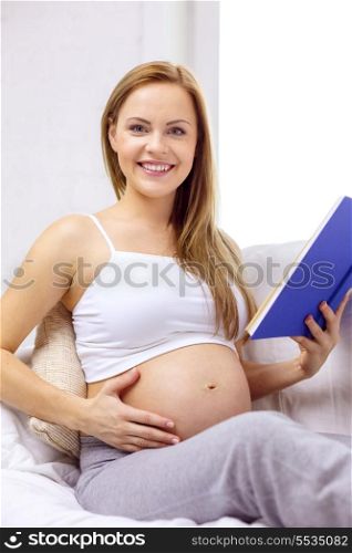 pregnancy and motherhood concept - smiling pregnant woman sitting on sofa and reading book at home