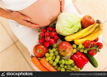 Pregnancy and nutrition - pregnant woman with a bowl of fruit and vegetables on her lap