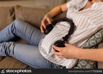 pregnancy and people concept - close up of pregnant woman with headphones on her belly at home. pregnant woman with headphones on her belly