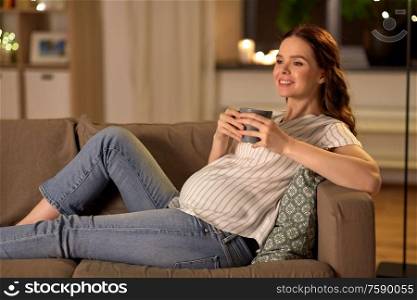 pregnancy and people concept - happy smiling pregnant woman drinking tea on sofa at home. smiling pregnant woman drinking tea at home