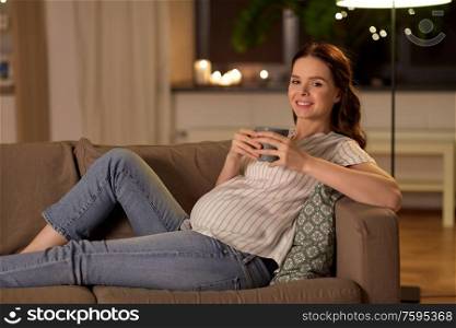 pregnancy and people concept - happy smiling pregnant woman drinking tea on sofa at home. smiling pregnant woman drinking tea at home