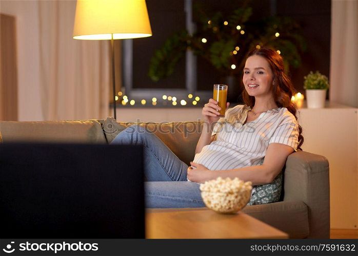 pregnancy and people concept - happy smiling pregnant woman on sofa watching tv at home. happy smiling pregnant woman watching tv at home