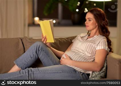 pregnancy and people concept - happy smiling pregnant woman reading book on sofa at home. happy smiling pregnant woman reading book at home
