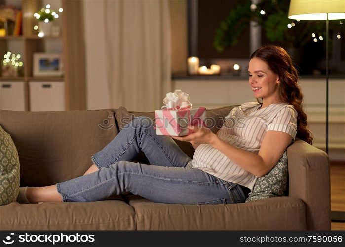 pregnancy and people concept - happy smiling pregnant woman with gift box on sofa at home. happy smiling pregnant woman with gift box at home