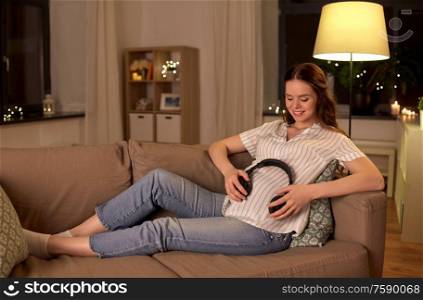 pregnancy and people concept - happy smiling pregnant woman with headphones on her belly at home. happy pregnant woman with headphones on her belly