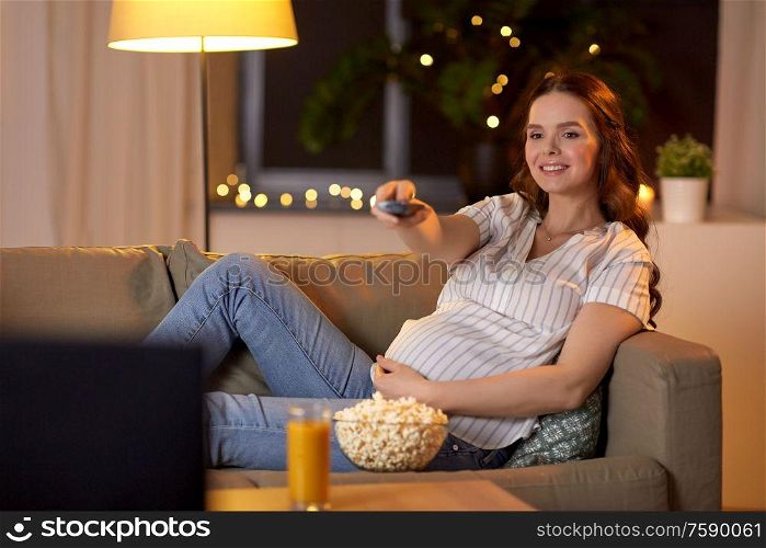 pregnancy and people concept - happy smiling pregnant woman with remote control watching tv at home. pregnant woman with remote control watching tv