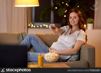 pregnancy and people concept - happy smiling pregnant woman with remote control watching tv at home. pregnant woman with remote control watching tv