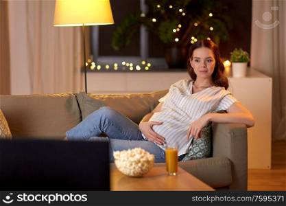 pregnancy and people concept - pregnant woman on sofa watching tv at home. pregnant woman watching tv at home