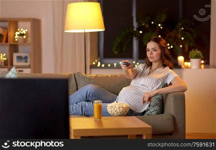 pregnancy and people concept - pregnant woman with remote control watching tv at home. pregnant woman with remote control watching tv
