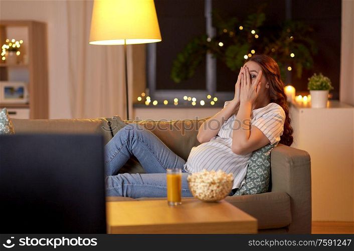pregnancy and people concept - scared pregnant woman on sofa watching tv at home. scared pregnant woman watching tv at home