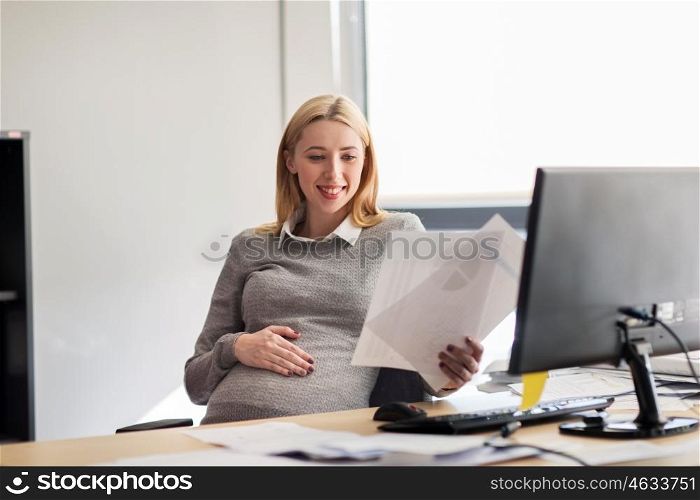 pregnancy, business, people and work concept - smiling pregnant businesswoman sitting at office table and reading papers