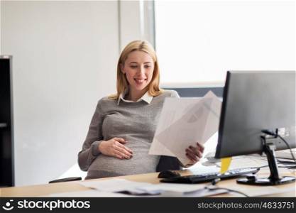 pregnancy, business, people and work concept - smiling pregnant businesswoman sitting at office table and reading papers