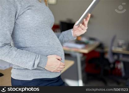 pregnancy, business, work and technology concept - close up of pregnant businesswoman with tablet pc computer at office. pregnant businesswoman with tablet pc at office