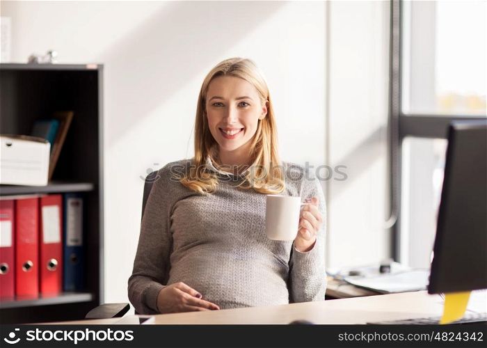 pregnancy, business, work and technology concept - smiling pregnant businesswoman with cup of tea at office