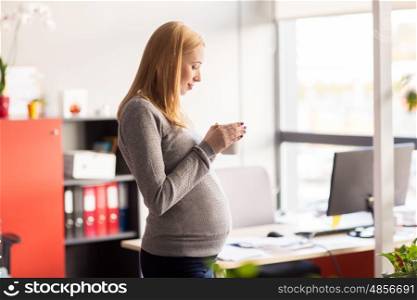 pregnancy, business, work and technology concept - smiling pregnant businesswoman with cup of tea at office