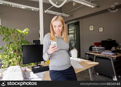 pregnancy, business, work and technology concept - smiling pregnant businesswoman with smartphone at office table