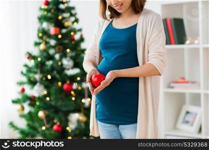 pregnancy, christmas and people concept - close up of pregnant woman with red heart on belly at home. close up of pregnant woman with heart at christmas