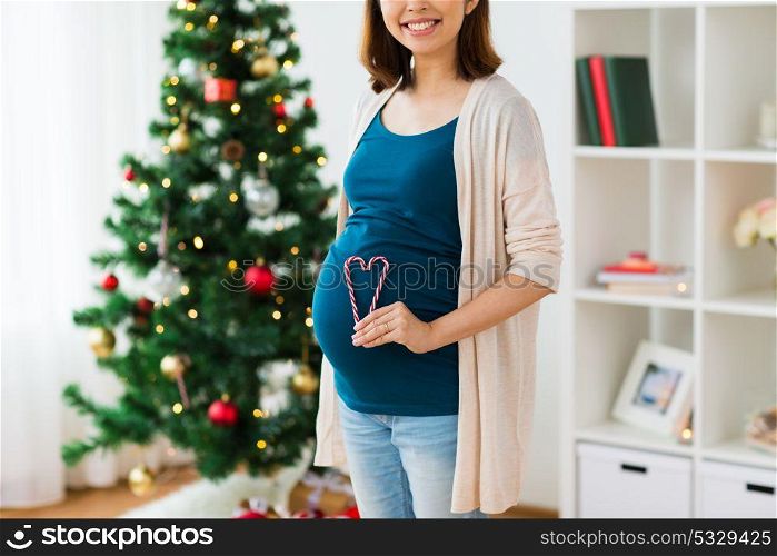 pregnancy, christmas and people concept - close up of pregnant woman with heart made of candy canes on belly at home. close up of pregnant woman with heart at christmas