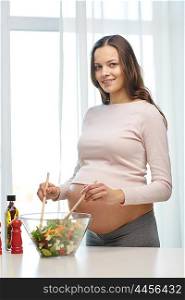 pregnancy, cooking food, healthy lifestyle, people and expectation concept - happy pregnant woman mixing vegetable salad in bowl at home