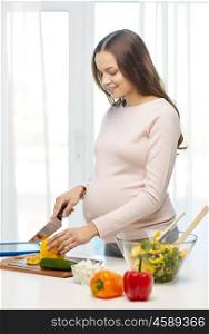 pregnancy, cooking food, healthy lifestyle, people and expectation concept - happy pregnant woman with knife chopping cucumber and preparing vegetable salad at home