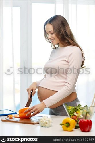 pregnancy, cooking food, healthy lifestyle, people and expectation concept - happy pregnant woman with knife chopping cucumber and preparing vegetable salad at home