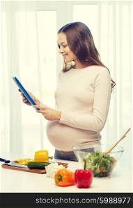 pregnancy, cooking food, healthy lifestyle, people and technology concept - happy pregnant woman with tablet pc computer preparing vegetable salad at home