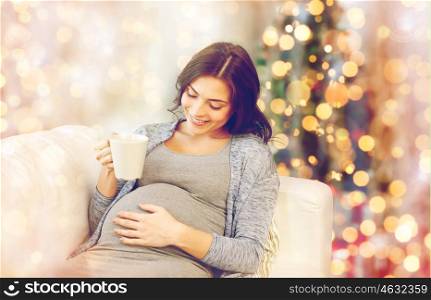 pregnancy, drinks, holidays, people and expectation concept - happy pregnant woman with cup drinking tea over christmas lights background