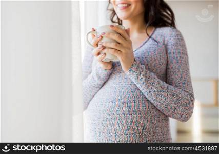 pregnancy, drinks, rest, people and expectation concept - close up of happy pregnant woman with cup drinking tea looking through window at home