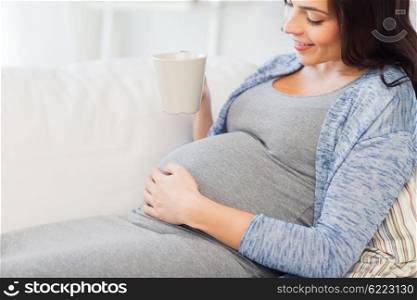 pregnancy, drinks, rest, people and expectation concept - close up of happy pregnant woman with big belly holding cup and drinking tea at home