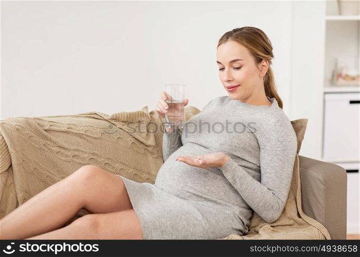 pregnancy, drinks, rest, people and expectation concept - happy pregnant woman with water and pills at home. happy pregnant woman with water and pills at home