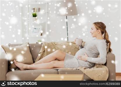 pregnancy, drinks, rest, people and expectation concept - happy pregnant woman with cup drinking tea at home over snow. happy pregnant woman with cup drinking tea at home