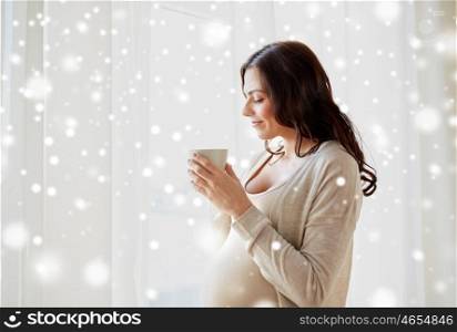 pregnancy, drinks, winter, people and expectation concept - happy pregnant woman with cup drinking tea at home over snow