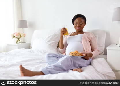 pregnancy, eating and people concept - happy african american pregnant woman with croissant buns at home. happy pregnant woman with croissant buns at home