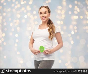 pregnancy, ecology, people and housing concept - happy pregnant woman with green house over holidays lights background. happy pregnant woman with green house