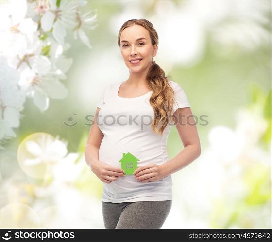 pregnancy, ecology, people and housing concept - happy pregnant woman with green house over natural spring cherry blossom background. happy pregnant woman with green house