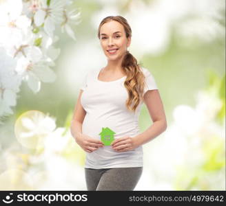 pregnancy, ecology, people and housing concept - happy pregnant woman with green house over natural spring cherry blossom background. happy pregnant woman with green house