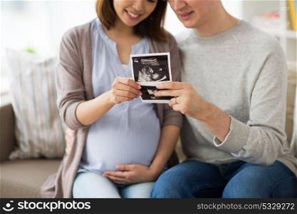 pregnancy, family and people concept - close up of happy man with his pregnant wife looking at baby ultrasound images at home. couple with baby ultrasound images at home