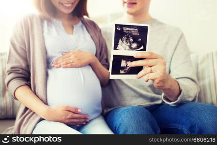pregnancy, family and people concept - close up of happy man with his pregnant wife looking at baby ultrasound images at home. close up of couple with baby ultrasound images