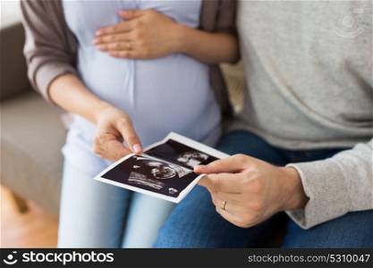 pregnancy, family and people concept - close up of man with his pregnant wife looking at baby ultrasound images at home. close up of couple with baby ultrasound images