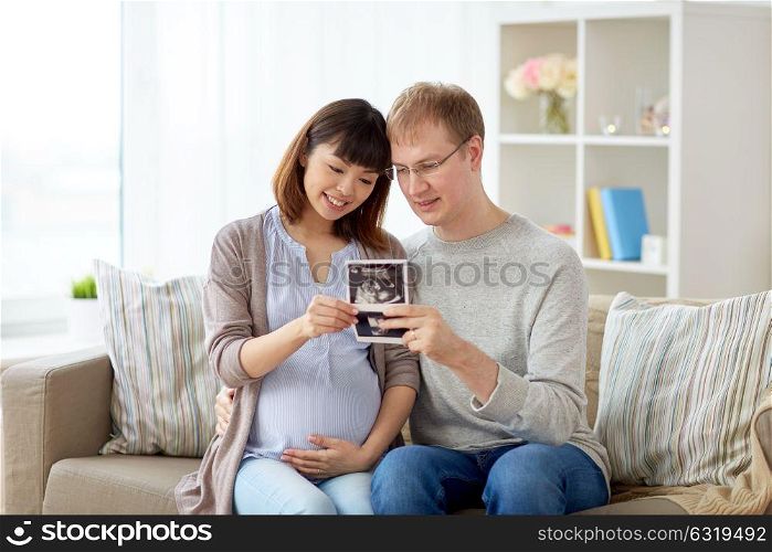 pregnancy, family and people concept - happy husband with his pregnant wife looking at baby ultrasound images at home. happy couple with ultrasound images at home
