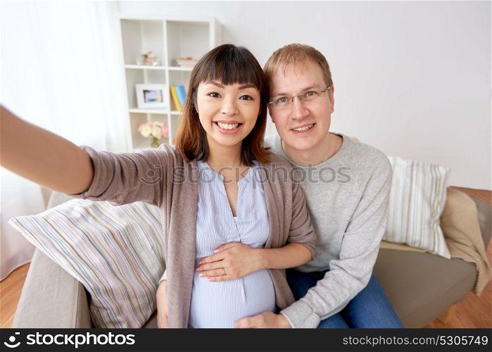 pregnancy, family and people concept - happy pregnant woman with husband taking selfie at home. pregnant woman with husband taking selfie at home