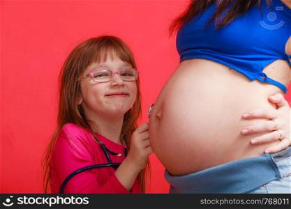 Pregnancy, family concept. Daughter using stethoscope on her pregnant mother belly to hear sibling heart tones. Daughter using stethoscope on pregnant mother