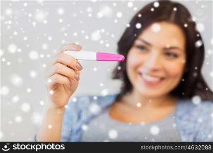 pregnancy, fertility, maternity and people concept - close up of happy smiling woman looking at pregnancy test at home over snow