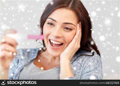pregnancy, fertility, maternity, emotions and people concept - happy smiling woman looking at pregnancy test at home over snow